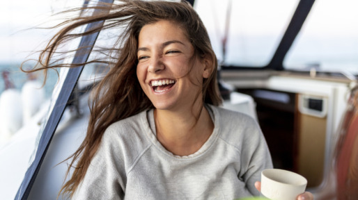 happy and young woman on a sail boot drinking hot tea in the morning