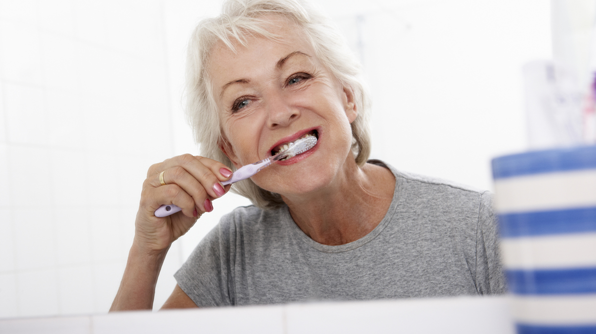 Senior Woman In Bathroom Brushing Teeth