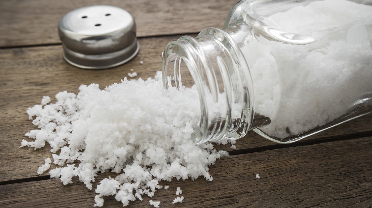 Spilled salt with salt shaker on wooden background