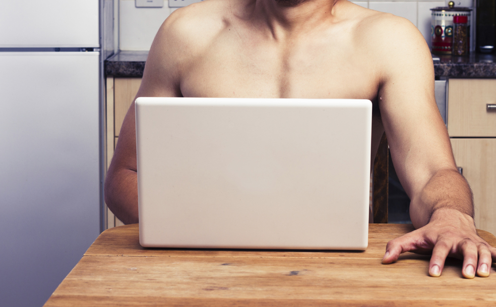 Young naked man watching porn in his kitchen