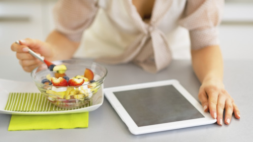Closeup on young woman with tablet pc eating fruit salad