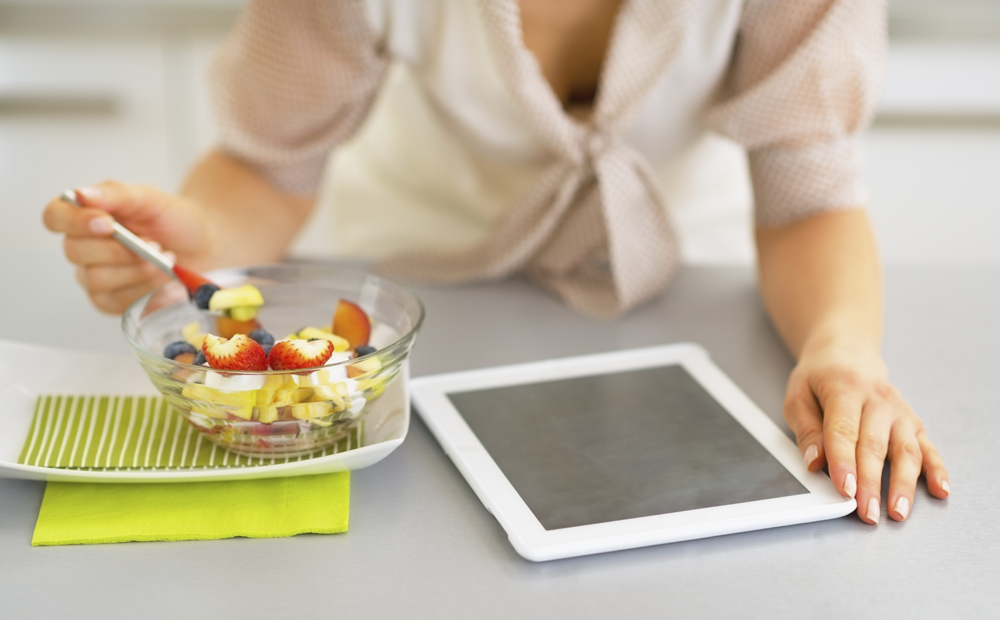 Closeup on young woman with tablet pc eating fruit salad