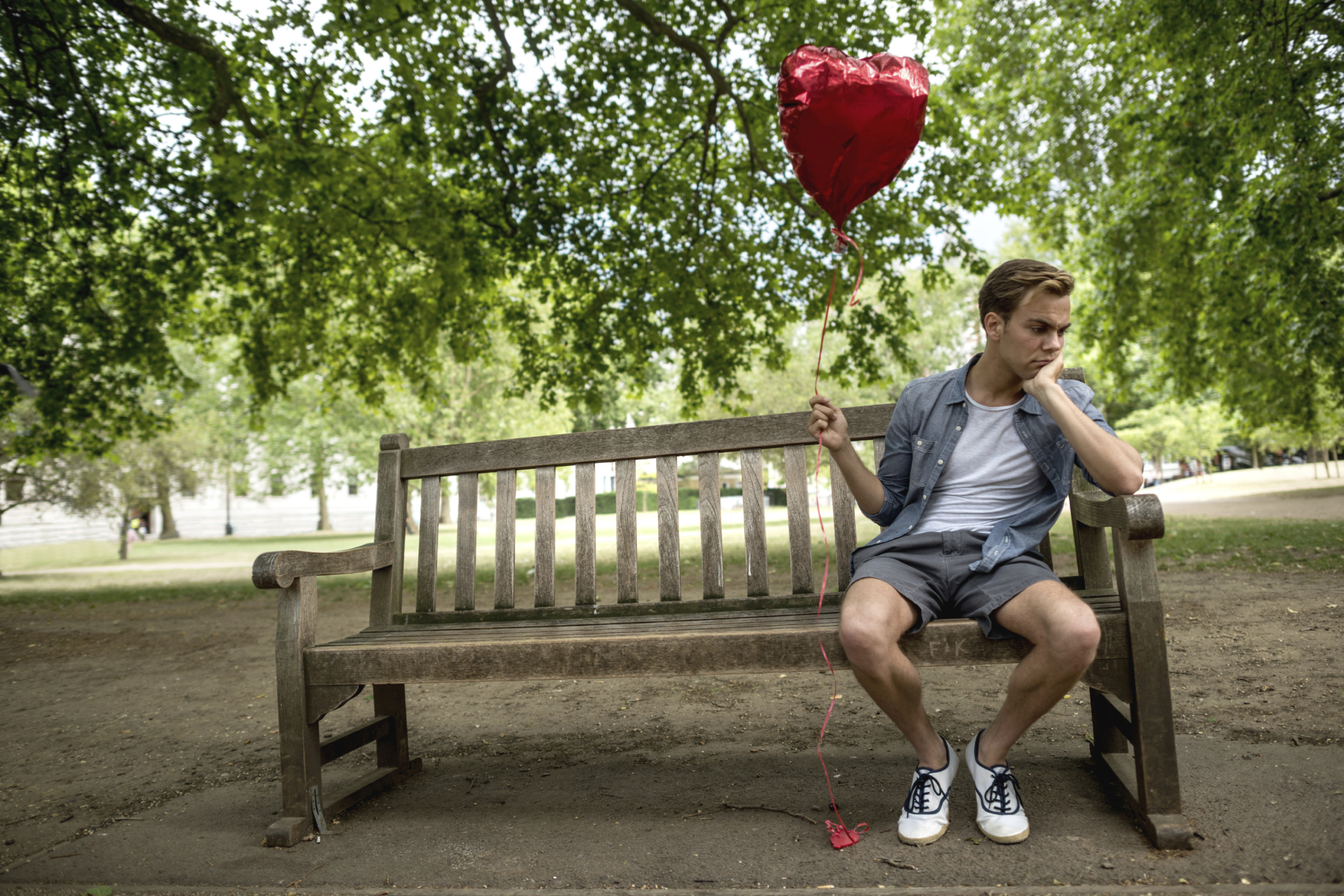 Heartbroken man at the park holding a heart shaped balloon