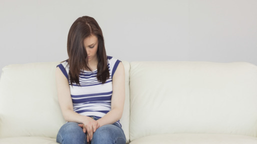 Depressed brunette sitting idly on a sofa looking the floor