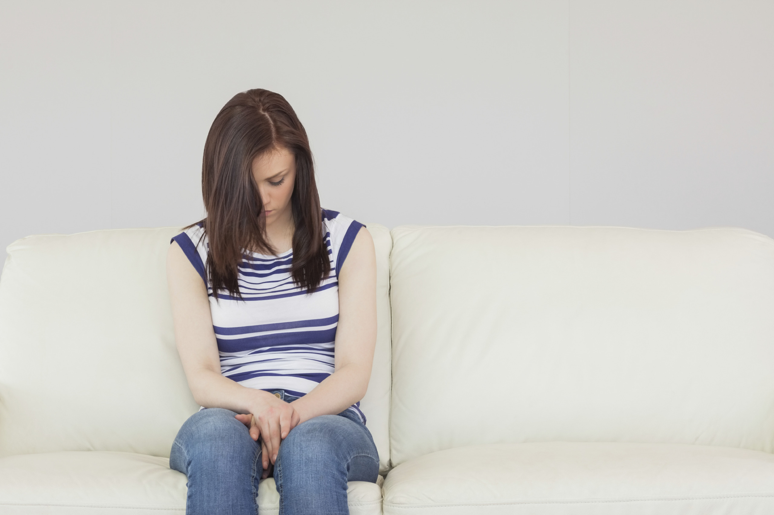 Depressed brunette sitting idly on a sofa looking the floor