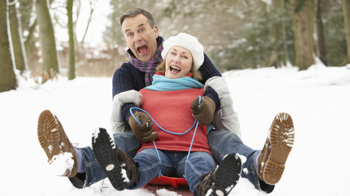 Senior Couple Sledging Through Snowy Woodland