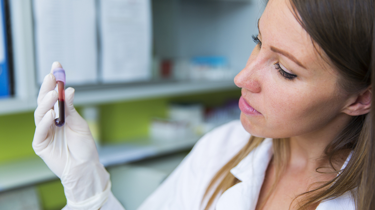 Cute young woman doctor holding vial with blood sample