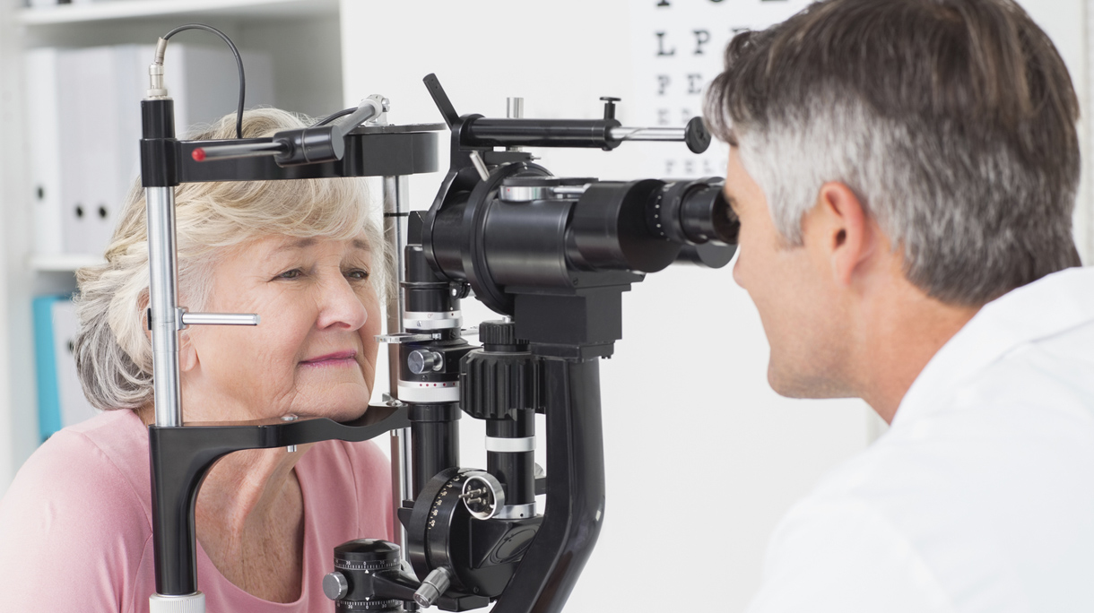 Optician examining senior female patient through slit lamp