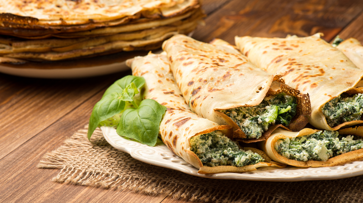 Pancakes filled  with spinach and cheese  on the wooden surface.