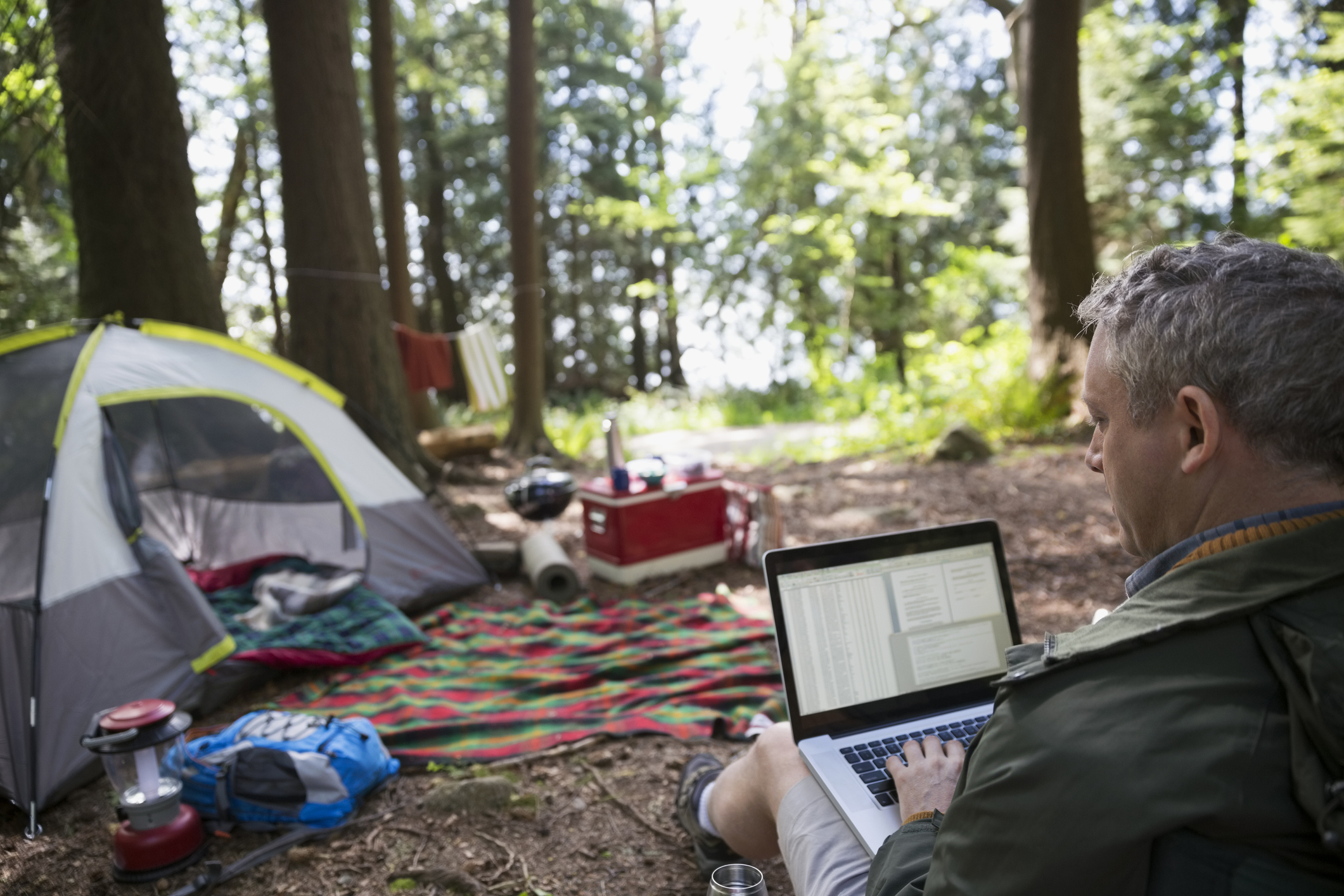 Man using laptop at campsite in woods
