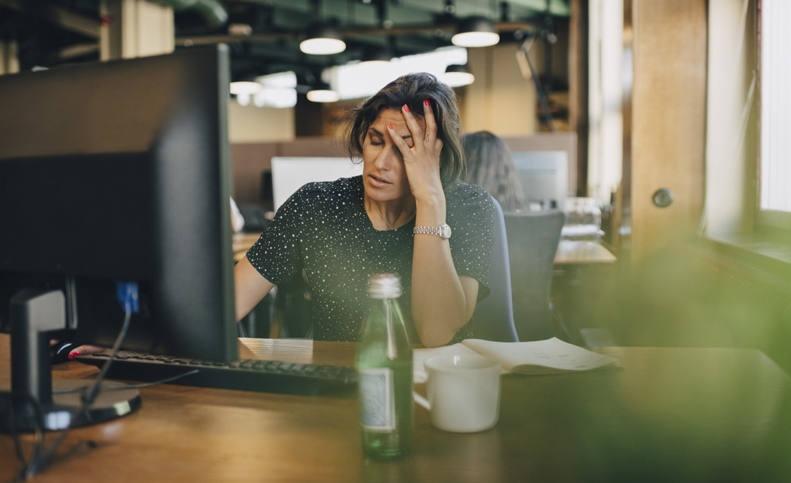 Tired businesswoman with head in hand sitting at computer desk in office