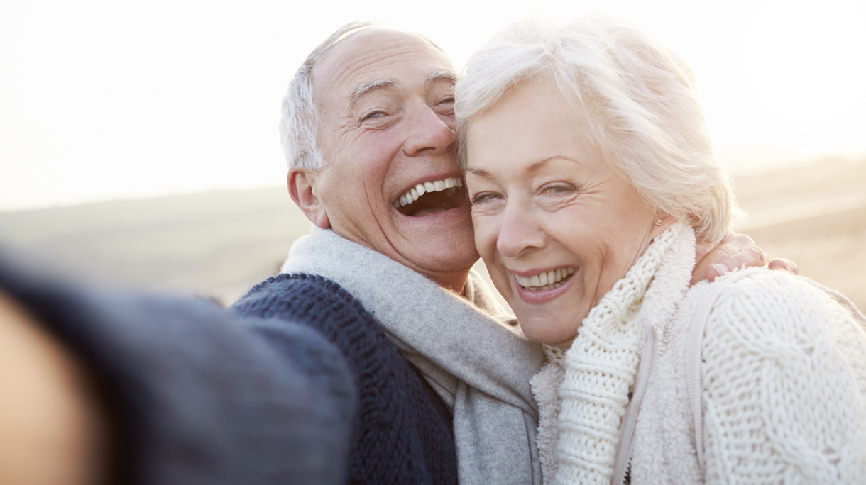 Senior Couple Standing On Beach Taking Selfie