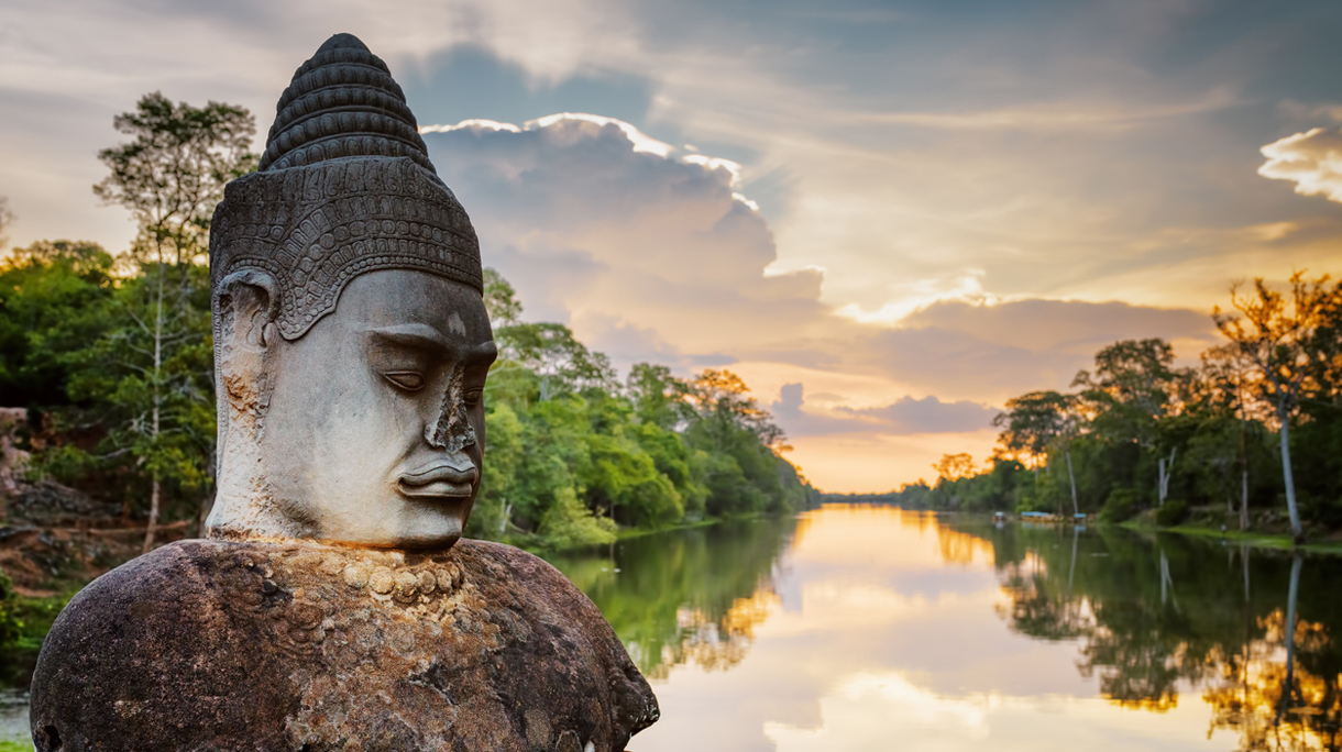 Stone Asura and sunset over moat surrounding Angkor in Cambodia