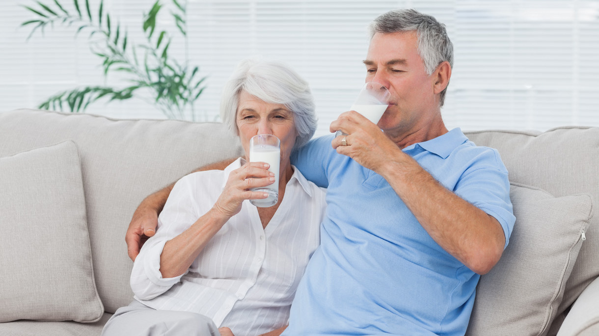 Couple drinking glasses of milk sitting on the couch