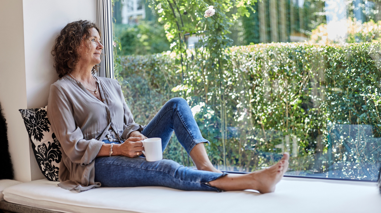 Vrouw met kop koffie op zitvensterbank ik haar woning