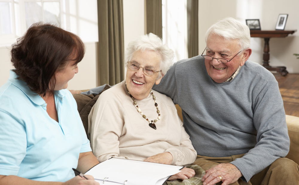 Senior Couple In Discussion With Health Visitor At Home