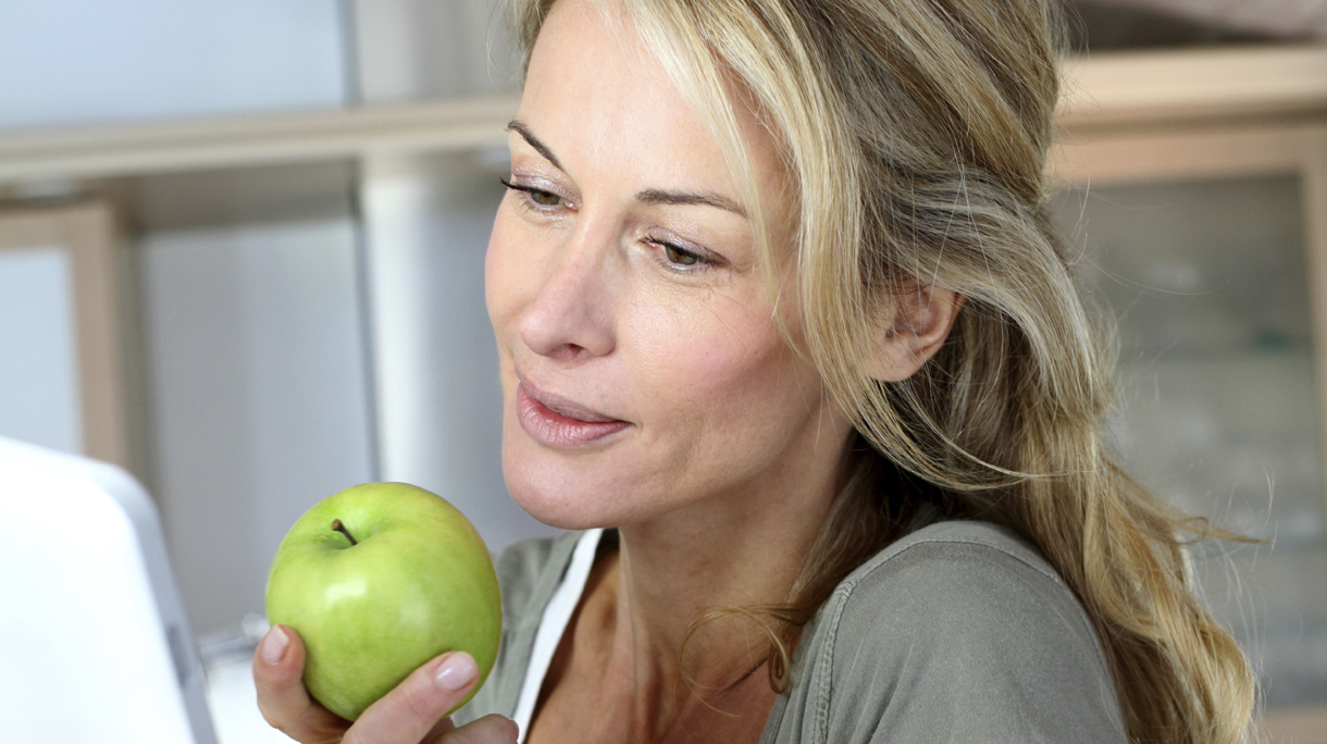 Cheerful adult woman websurfing with tablet and eating apple
