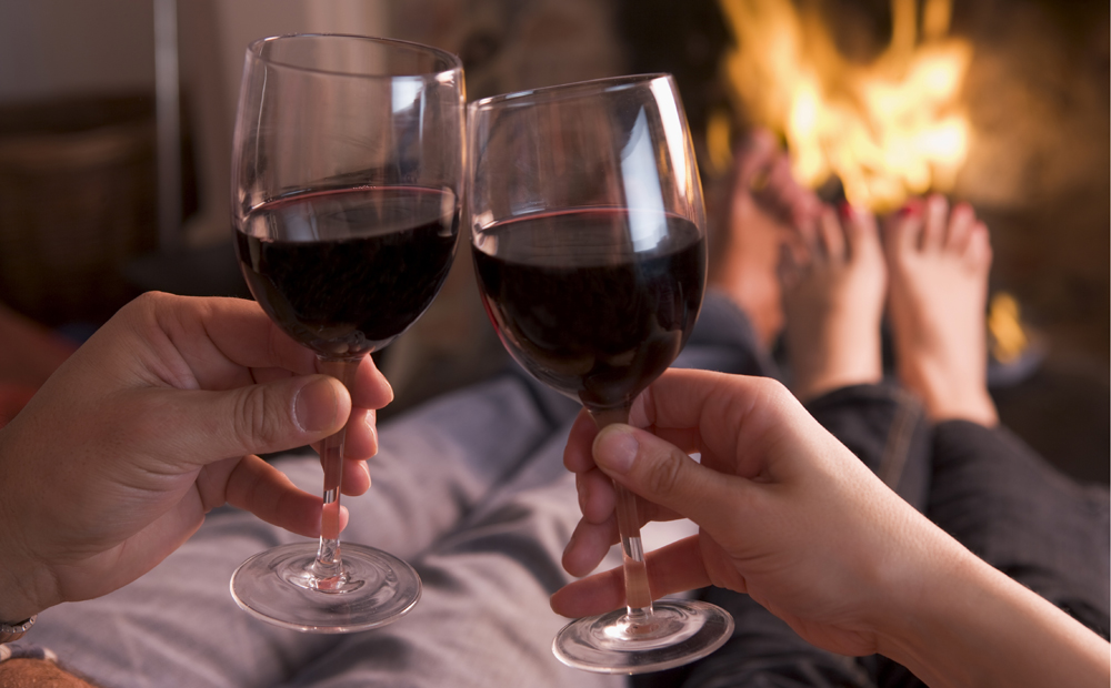 Feet warming at fireplace with hands holding wine