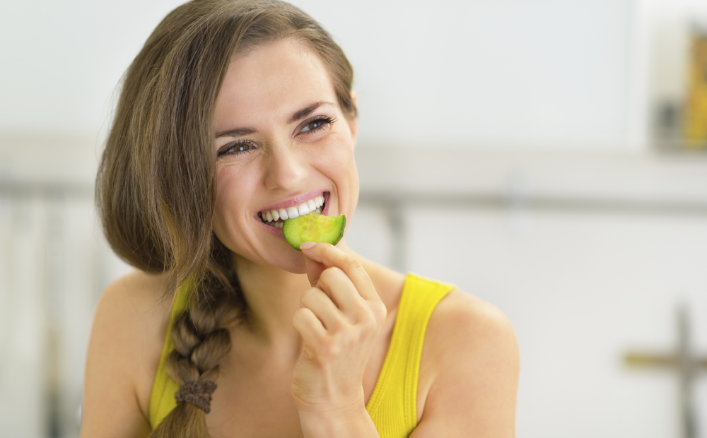 Portrait of young woman eating cucumber in kitchen
