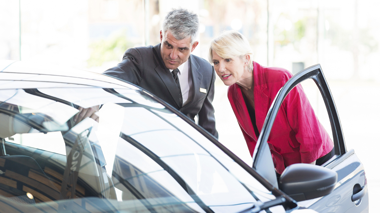 mid age salesman showing new car to customer