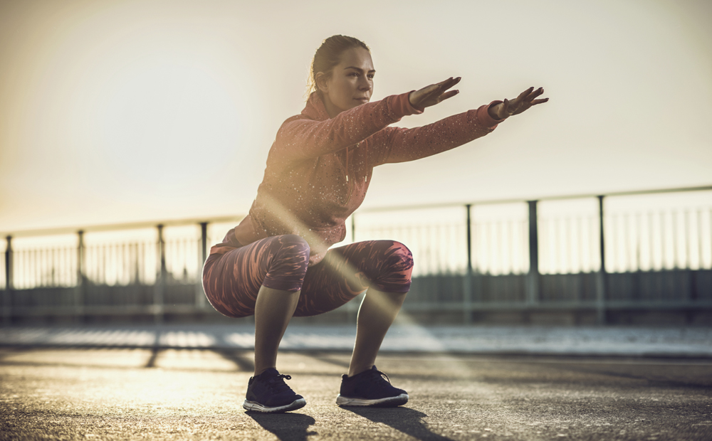 Young woman doing squats on a road at sunset.