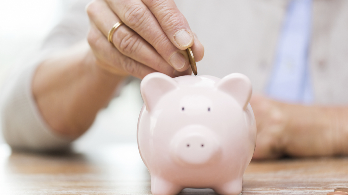 senior woman hand putting money to piggy bank