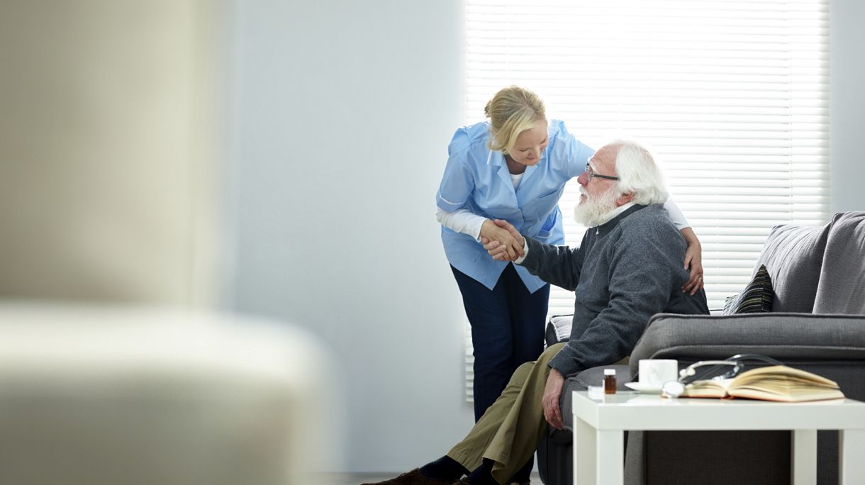 Female caregiver helping senior man get up from couch
