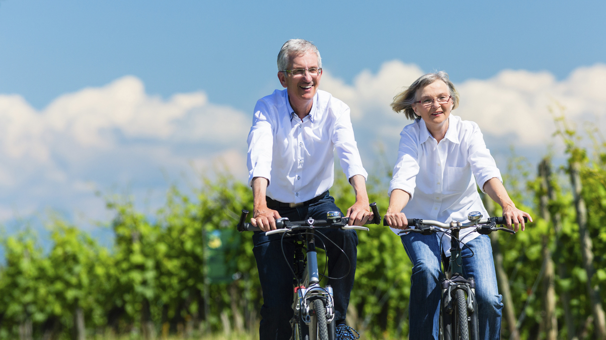 Senior woman and man  using bike in summer in vineyard