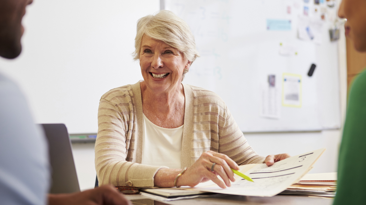 Senior teacher at desk talking to adult education students