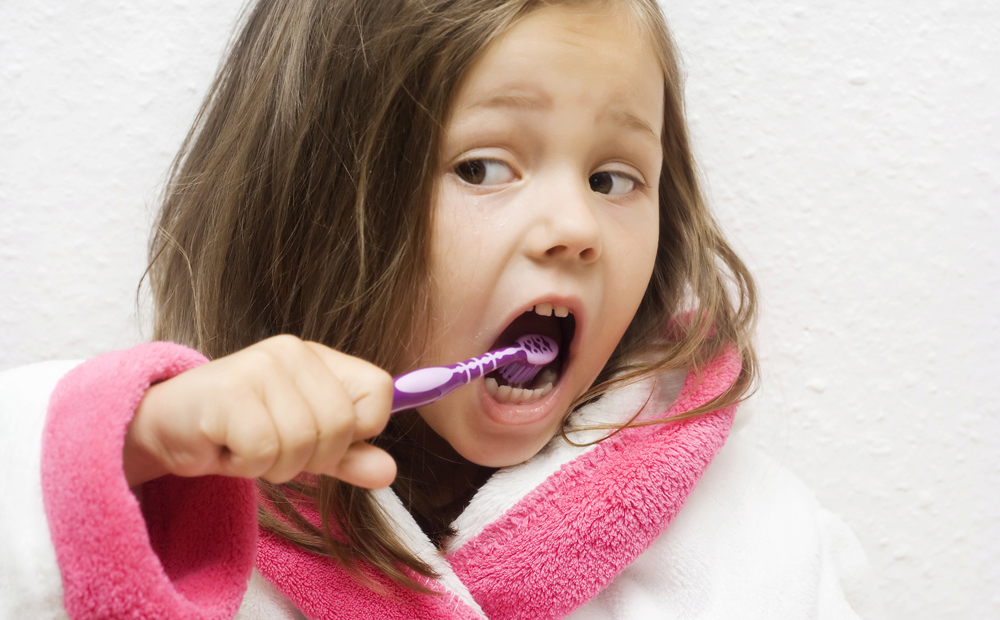 little girl wearing a bathrobe brushing her teeth