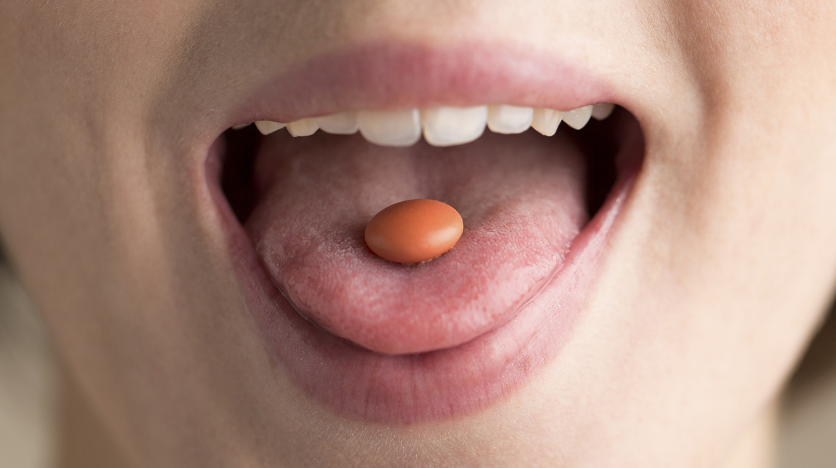 Young woman with pill in mouth