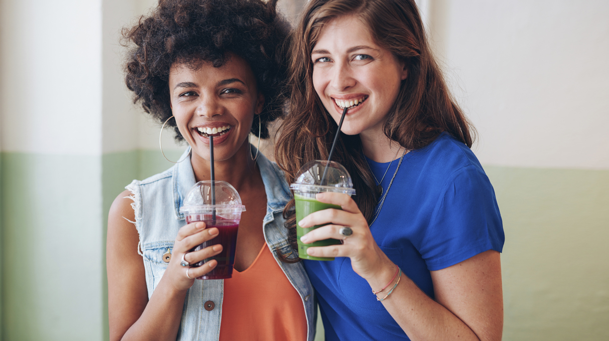 Two young friends drinking fresh fruit juice