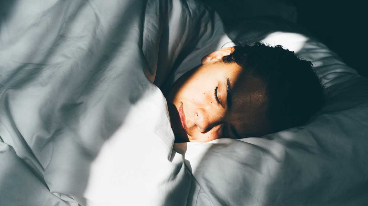 Vrouw ligt lekker te slapen in haar bed in het ochtendzonnetje