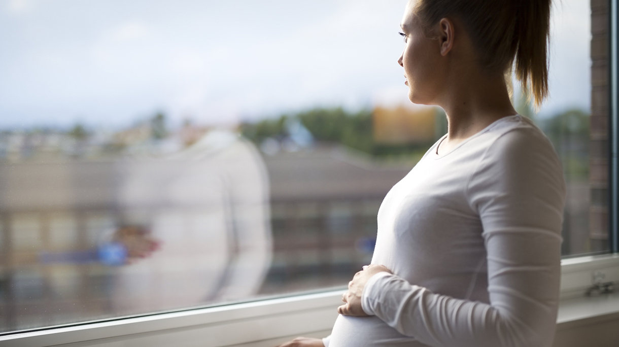 Thoughtful pregnant woman looking out the window