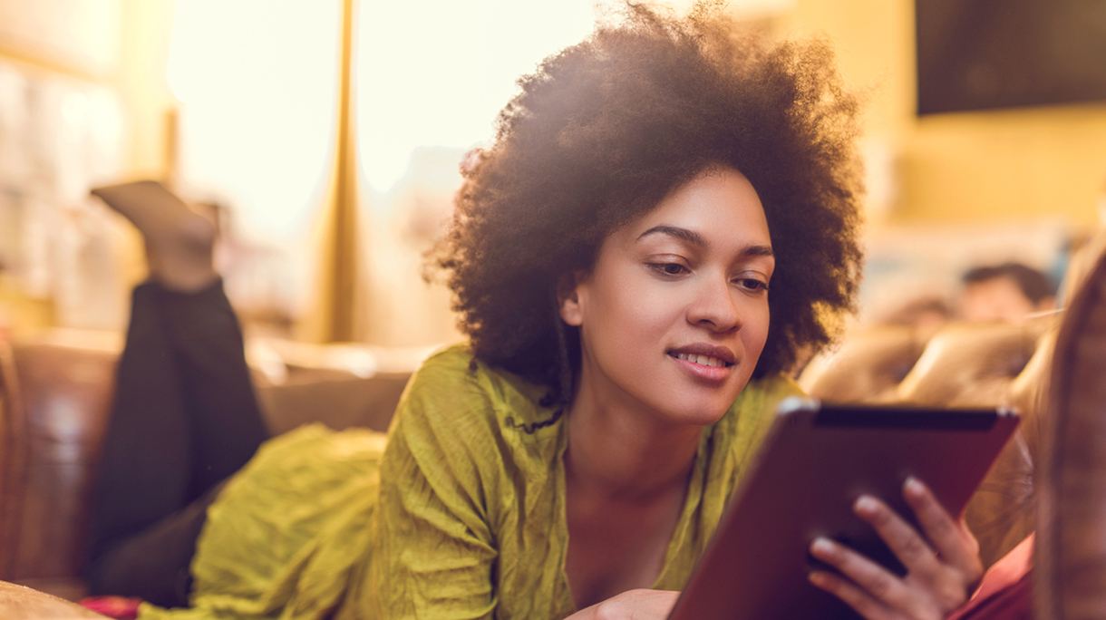 African American woman reading something from e-reader at home.