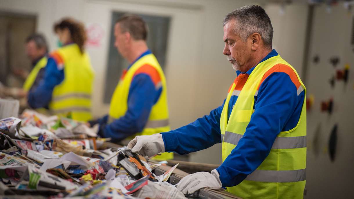 Group of workers sorting papers at recycling plant