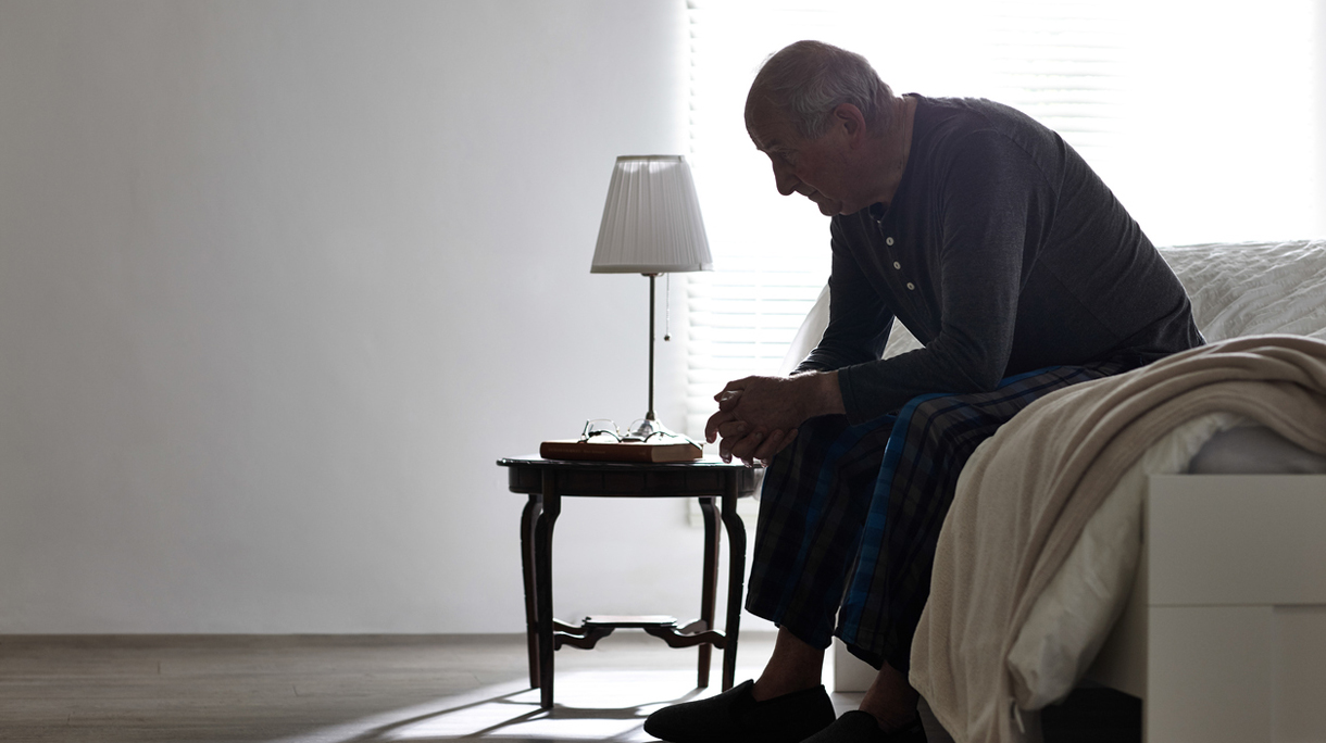 Elderly man sitting on bed looking serious
