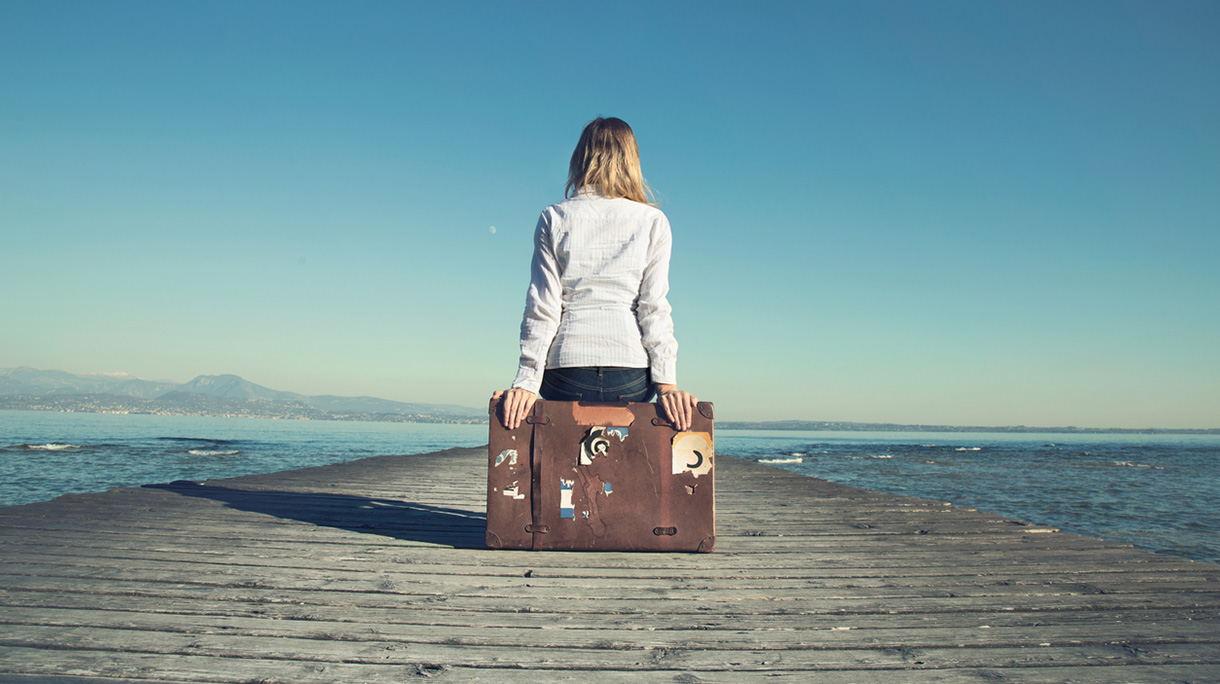 woman sitting on her suitcase waiting for the sunset