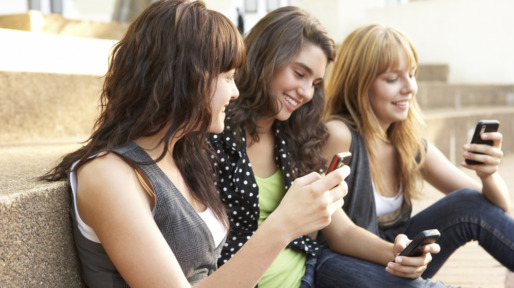 Group Of Teenage Students Sitting Outside On College Steps Using Mobile Phone