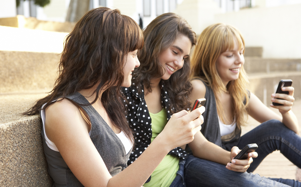 Group Of Teenage Students Sitting Outside On College Steps Using Mobile Phone