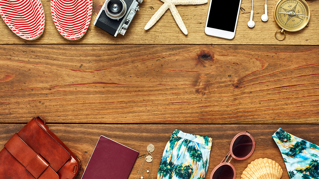 Flat lay of travel and beach accessories on wooden floor