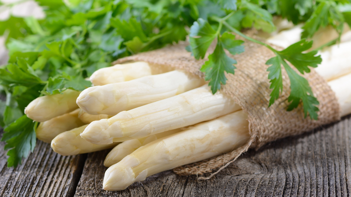 Clump of white asparagus with leaves on a wooden surface