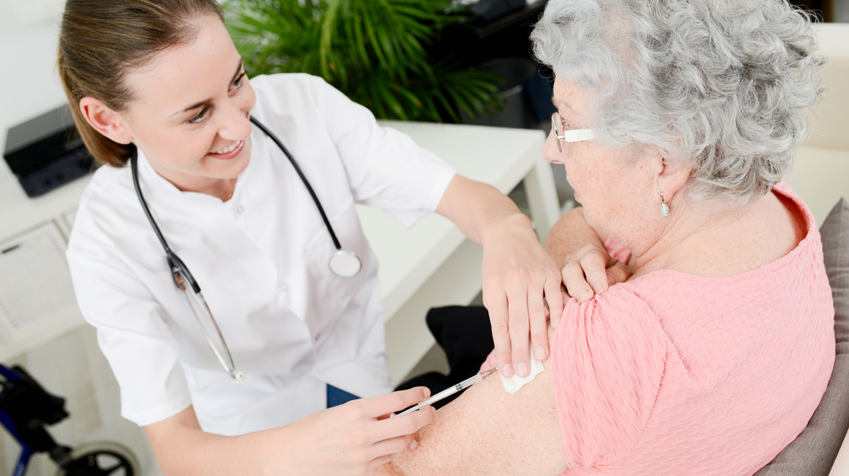 cheerful young nurse giving vaccine injection to elderly woman home