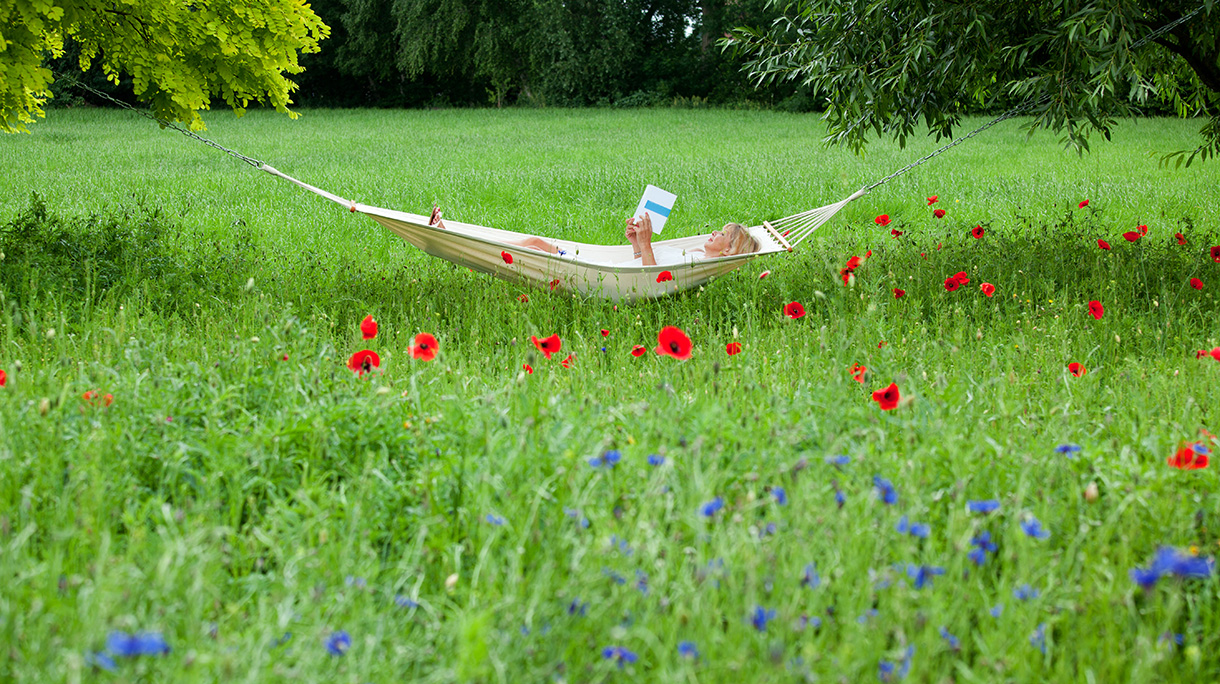 Mature woman lying on hammock in garden reading book