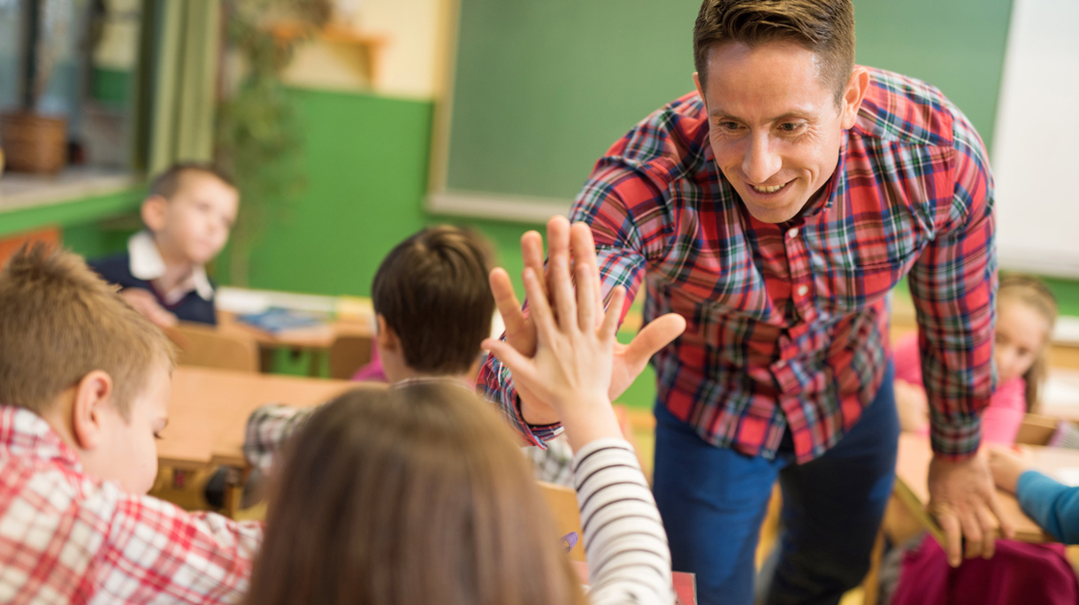 Happy elementary teacher congratulating his student on good answer.