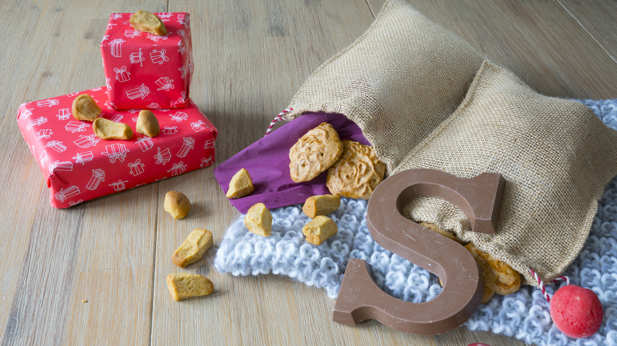 wooden table with Dutch Sinterklaas snacks in jute bag, with knitted napkin, taai taai, gifts