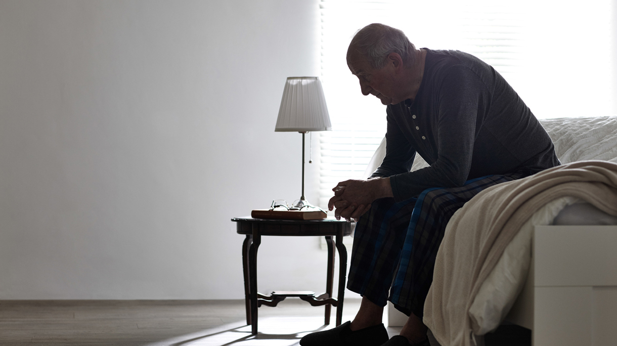 Elderly man sitting on bed looking serious