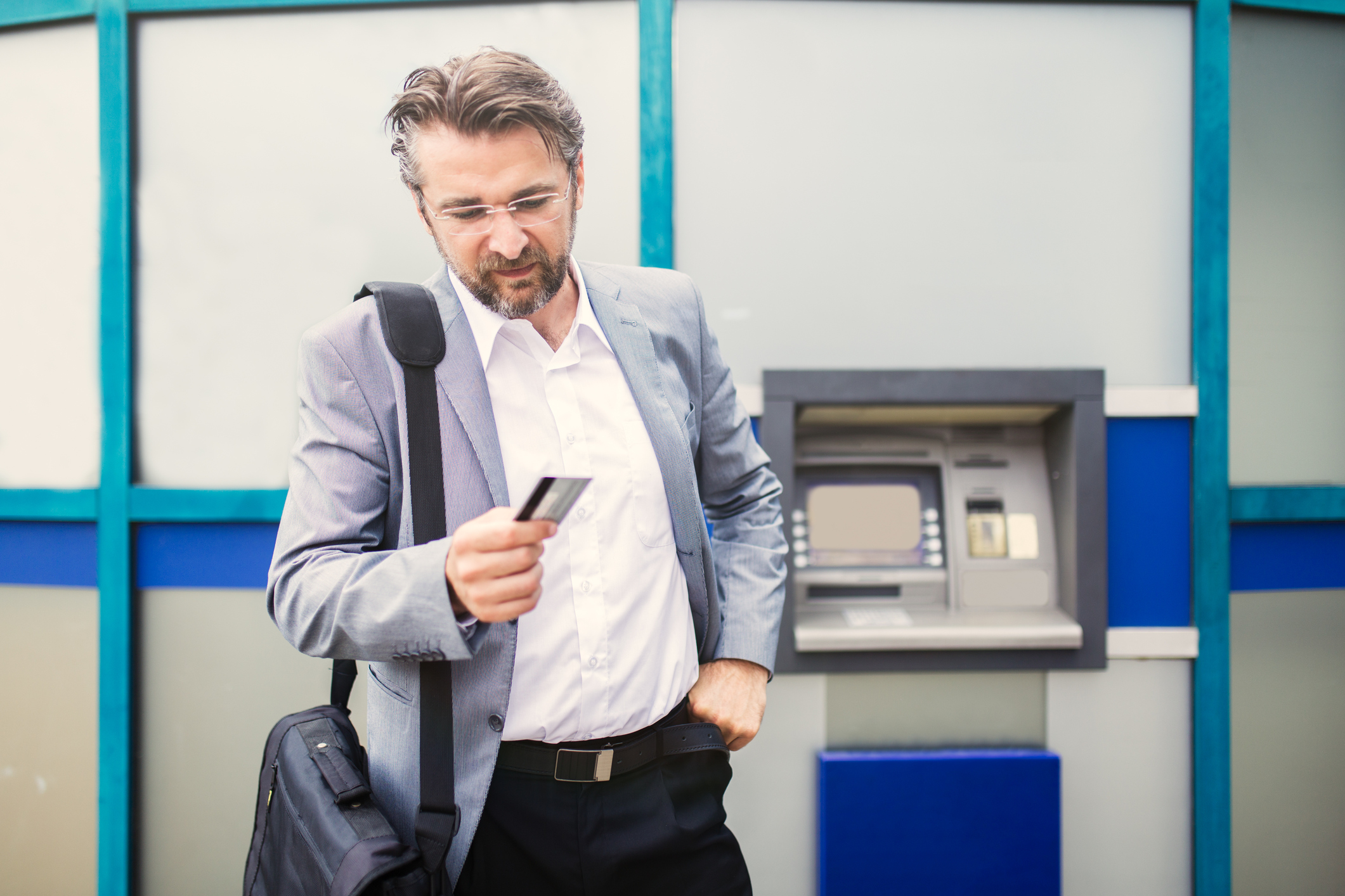 Businessman with rejected credit card next to cash machine.