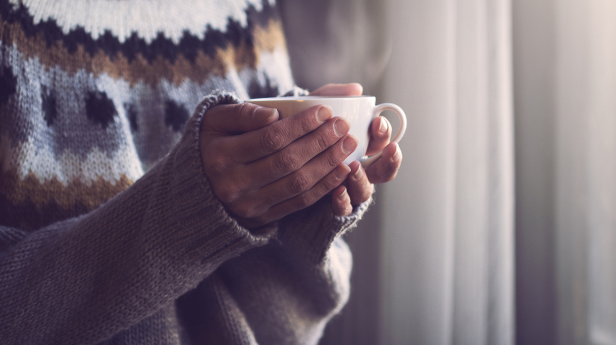 Woman in knitted sweater hands holding cup of warm coffee