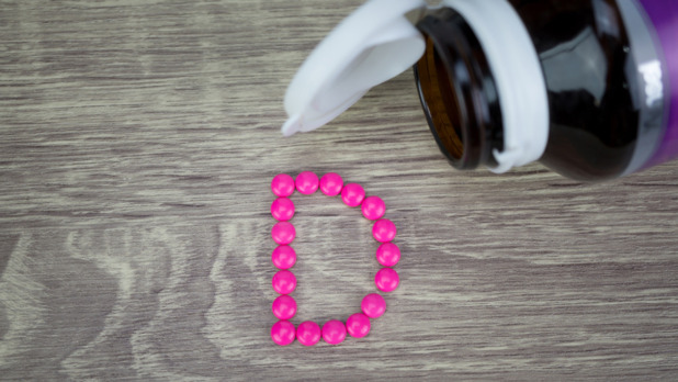 Pink pills forming shape to D alphabet on wood background